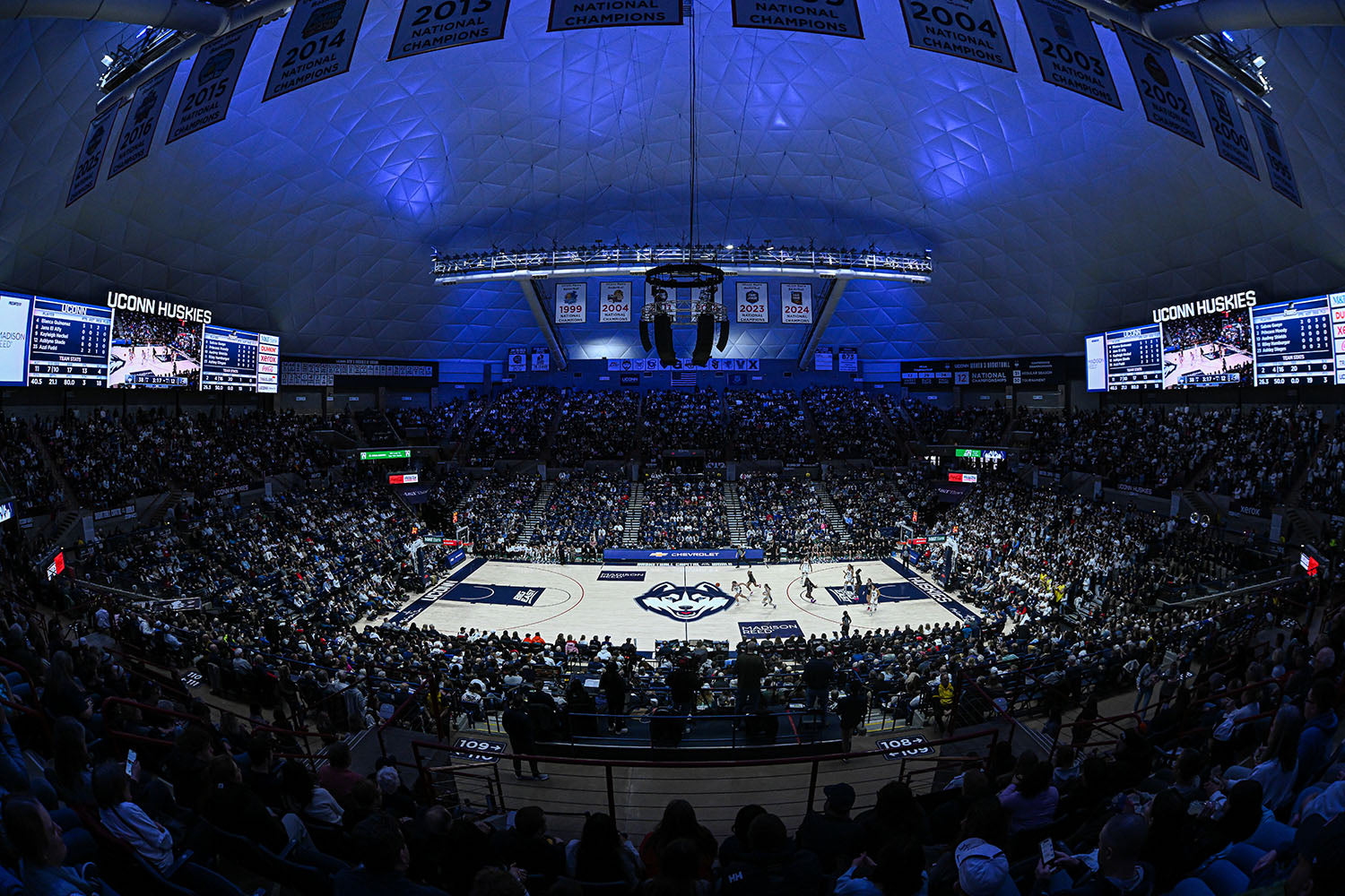 Basketball game in progress inside a large indoor arena with fans and players on the court.