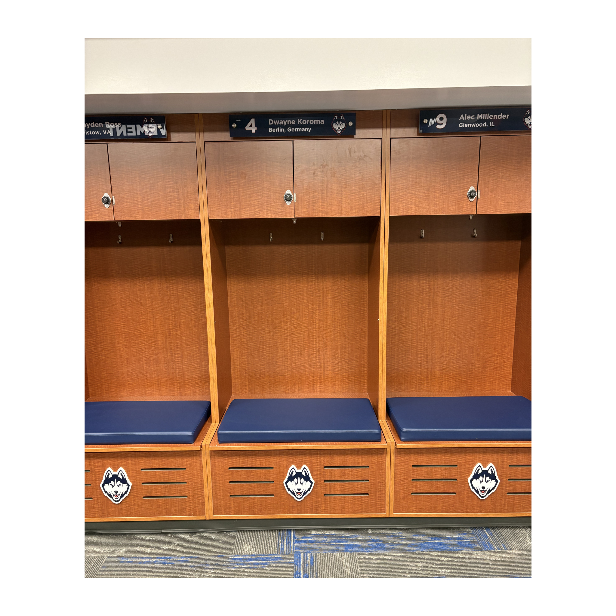 UConn wooden locker room lockers with blue seats and team logos on a white background